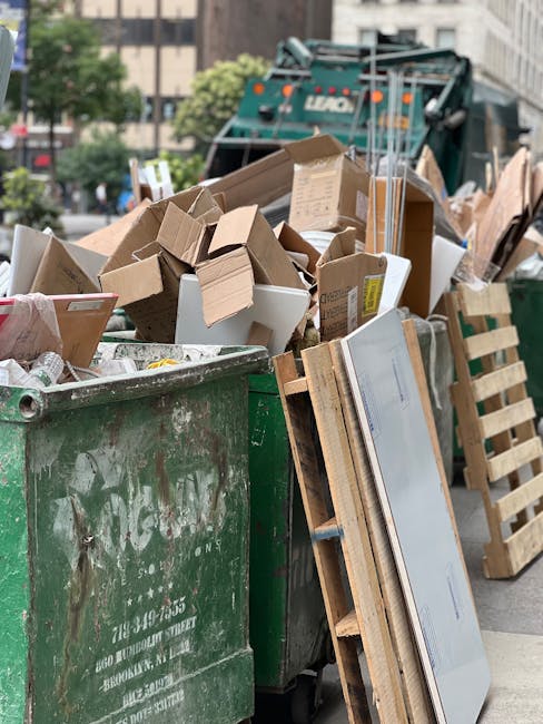 A large green waste disposal bin filled with a mixture of cardboard boxes, including some flattened and others partially intact, alongside pieces of packaging and paper. The cardboard varies in colour